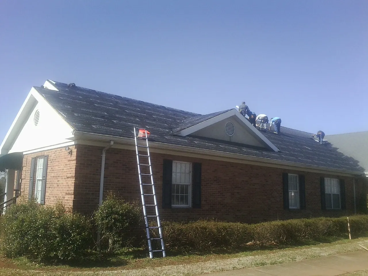 Crew tearing shingles off a brick ranch roof with a ladder set — Emergency Roof Repair work by our crew in Oswego