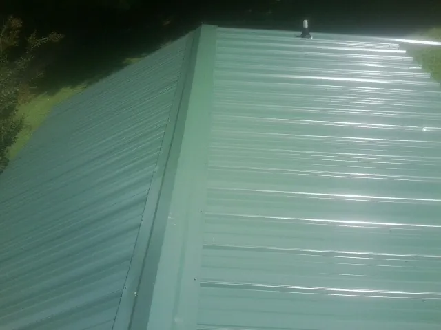 New green metal panels meeting at the ridge of a roof — Flat Roof Repair work by our crew in Oswego
