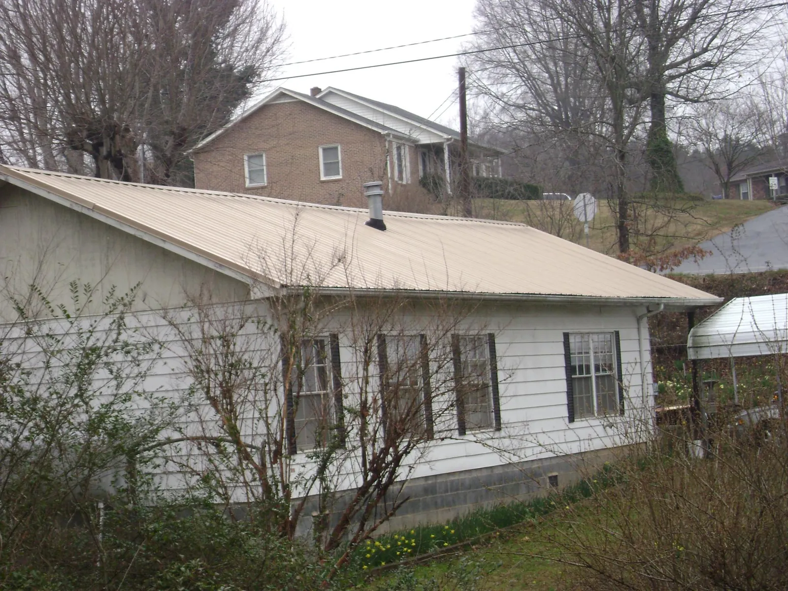 Tan metal roof on a white sided house set into a hillside — Commercial Roofing by Roofing Brothers in Oswego